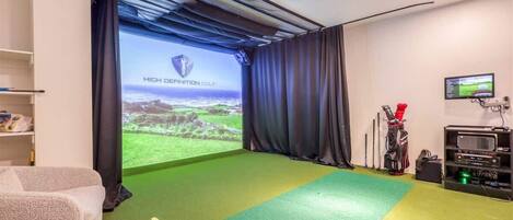 Una habitación con una pantalla grande mostrando 'HIGH DEFINITION GOLF', un bolso de golf y un proyector.