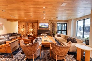 A cozy living room with a fireplace, wooden walls, and large windows offering a view. - Brand New Luxury Amenities Frontgate Residence (Avon)