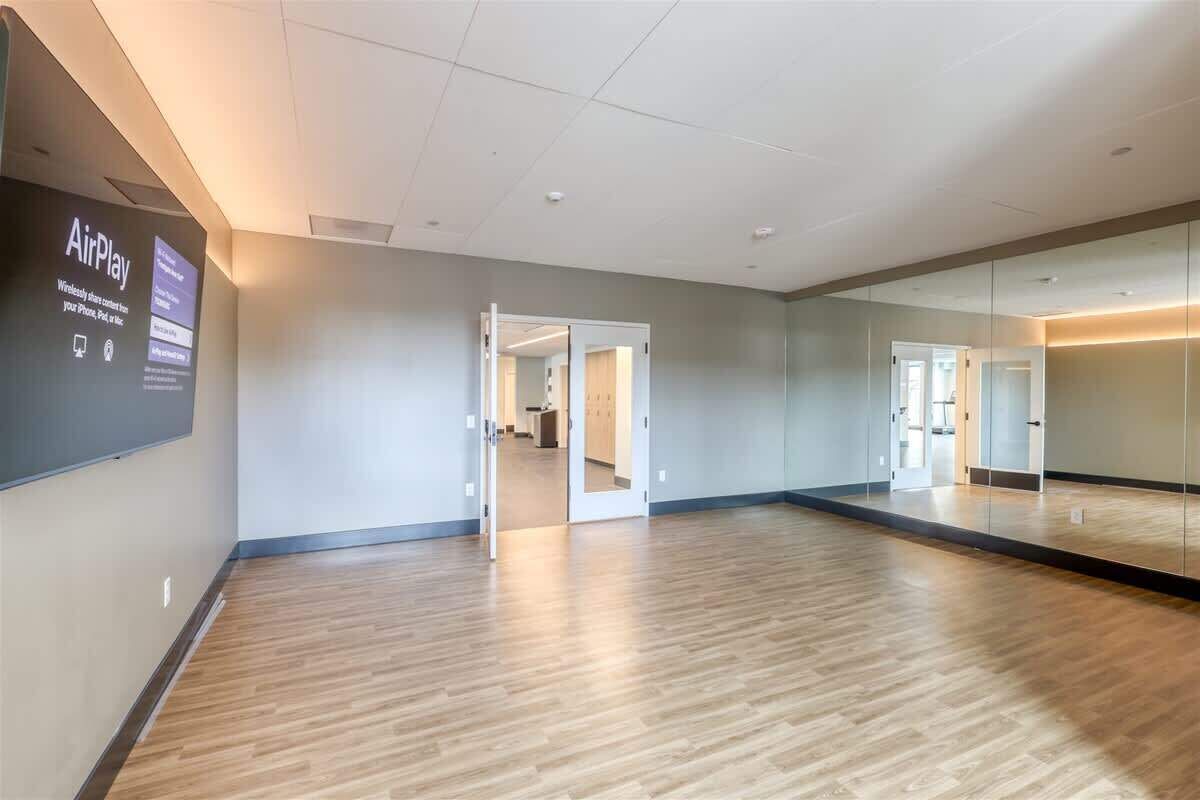 A spacious room with a wooden floor, a large mirror, and a wall-mounted screen displaying 'AirPlay'.