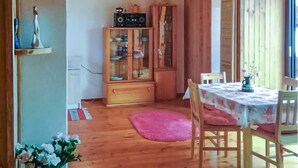 Un comedor con una mesa de madera, sillas, un tapete rosa y un mueble con puertas de vidrio.