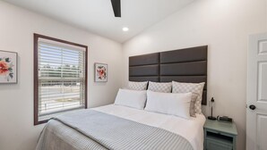 Un dormitorio con una cama grande, una mesita de noche, una ventana con persianas y una puerta.