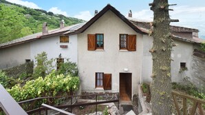 Une maison à deux étages avec une façade en pierre, des volets en bois et un escalier en pierre menant à l’entrée.