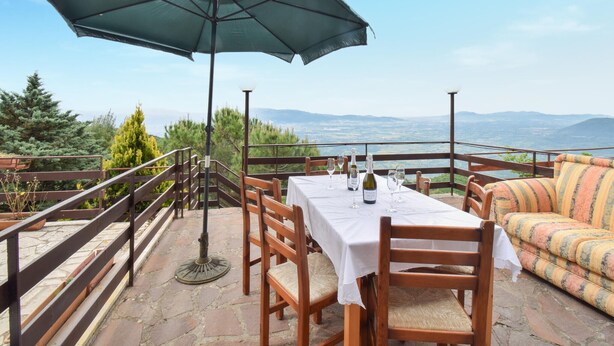 Une terrasse avec une table dressée pour le repas, un canapé et un parasol, offrant une vue sur un paysage magnifique.
