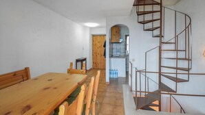 Un coin repas avec une table et des chaises en bois, un petit espace cuisine avec une porte en bois, et un escalier en colimaçon.