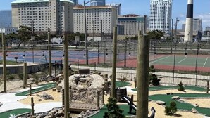 Un parc avec un petit étang, des structures en bois et un phare en arrière-plan.