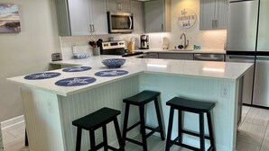 A modern kitchen with a large island, grey cabinets, stainless steel appliances, and a herringbone tile backsplash.