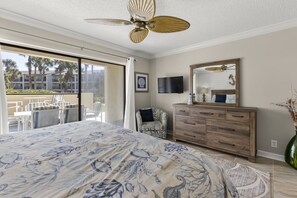 A bedroom with a large bed, a ceiling fan, a TV, a dresser, and a sliding glass door leading to an outdoor patio. - Beautifully Updated Ground Floor Condo Stops From The Pool And Beach Access! (St. Augustine)