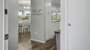 Una cucina moderna con mobili bianchi, un'area pranzo con sedie bianche e un'opera d'arte appesa al muro.
