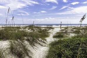 Un sentier bordé de sable et d’herbe qui mène à l’océan.