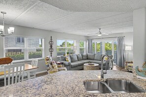 A spacious living area with a gray sofa, dining table, and a kitchen with granite countertops.