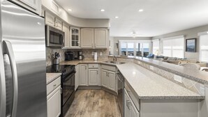 A modern kitchen with a stainless steel refrigerator, microwave, and stove, light-colored cabinets, and a large island with a sink. - The best Views On The Beach From This 3rd Floor Oasis!! (St. Augustine)