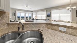 A kitchen with granite countertops, stainless steel sink, and a ceiling fan. - The best Views On The Beach From This 3rd Floor Oasis!! (St. Augustine)