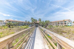 Une promenade en bois menant à un bâtiment doté de nombreux balcons et bordé de palmiers.