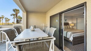 Ein Balkon mit Esstisch und Stühlen, ein Bett mit Blick und Palmen im Hintergrund.