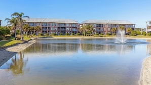 Un hotel con un'ampia vasca d'acqua di fronte, circondato da palme e un cielo sereno.