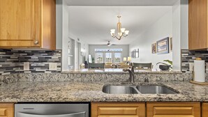 Cucina con piani di lavoro in granito, lavello in acciaio inossidabile, mobili in legno e lampadario.
