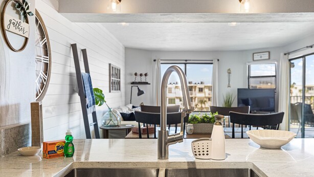 A modern kitchen with a stainless steel sink, a dining area with a TV, and a view of buildings outside. - Stunning views from this top floor three bedroom condo! (Saint Augustine)