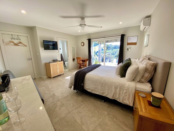 A bedroom with a bed, a desk, a chair, a TV, and a view of the outdoors.