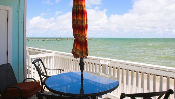 Ein blauer Tisch und Stühle auf einem Balkon mit Blick auf das Meer und einen Steg.