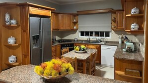 A kitchen with wooden cabinets, a stainless steel refrigerator, a granite countertop, and a dining table with chairs. - Spring House AL (Arco da Calheta)