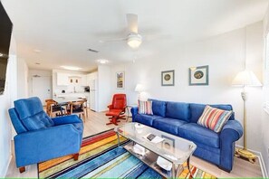 Un salon moderne avec un canapé bleu, un fauteuil rouge, une table basse en verre et un tapis rayé aux couleurs vives.