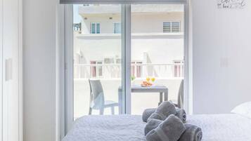 Habitación de hotel con cama, toallas, balcón con mesa y sillas, y vistas a edificios.