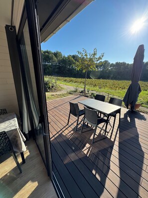 Een terras buiten met een tafel, stoelen, een parasol en uitzicht op een wijngaard.