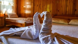 A wooden room with a bed, a window, and two towels arranged in a heart shape on the bed. - YAVUZ MOTEL ADRASAN (Kumluca)
