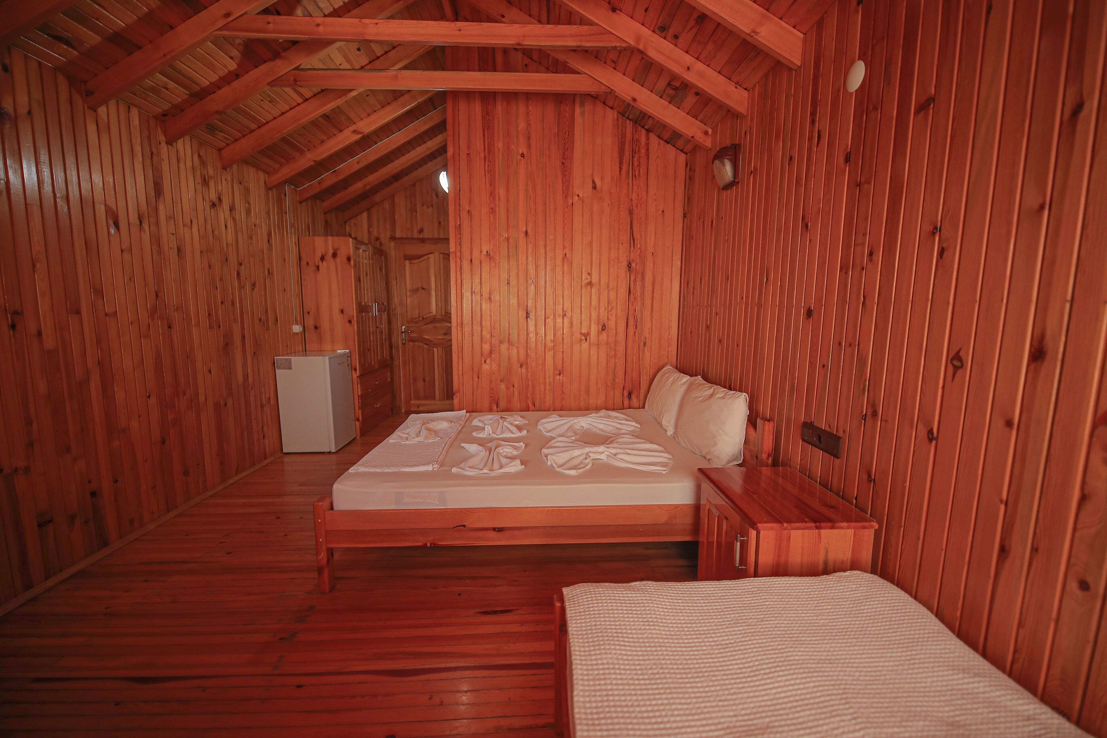 A wooden room with a bed, a small table, and a white cabinet.