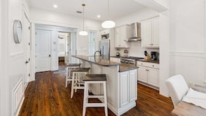 A spacious kitchen with white cabinetry, a central island with bar stools, and a modern stainless steel range hood.