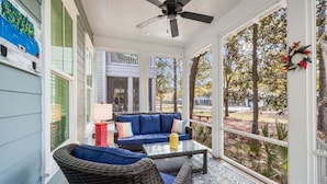 A covered porch with wicker furniture, a glass coffee table, and a view of the backyard.