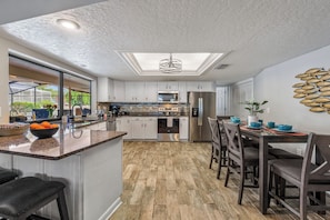 A modern kitchen with a central island, stainless steel appliances, and a dining area with a view of the outdoors. - 12 Min to AMI | Pool, Hot Tub & Arcade Game Room (Bradenton)