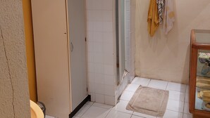 Un baño con suelo de baldosas blancas, un inodoro, un lavabo, un espejo y un perchero con toallas.