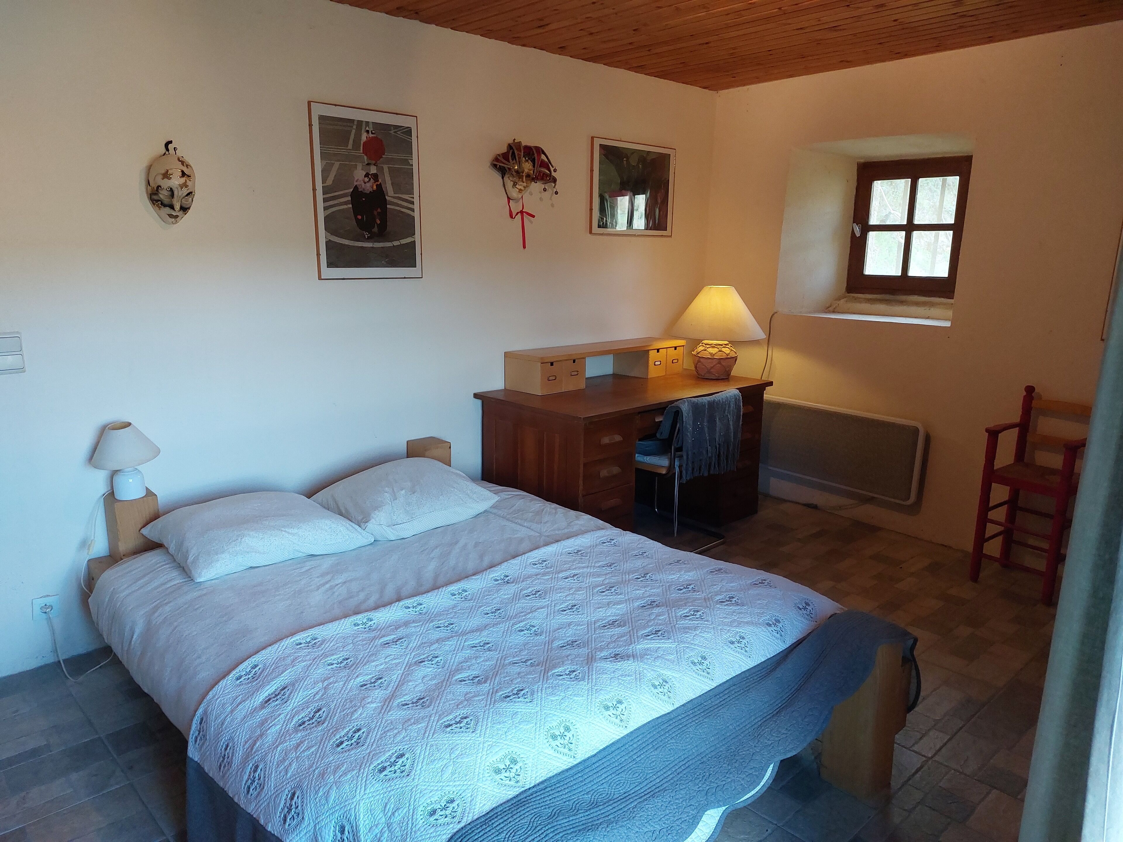 Une chambre à coucher avec un lit, un bureau avec une lampe, une chaise et une fenêtre.