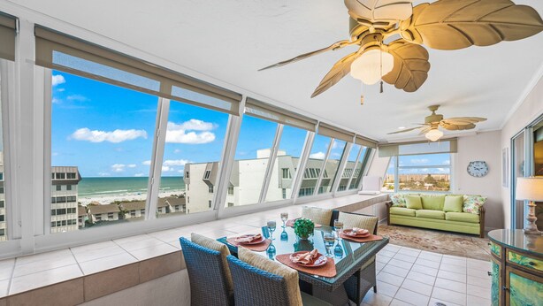 Un coin repas avec vue sur la plage, un ventilateur de plafond et un canapé vert.