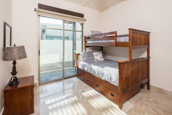 Une chambre avec un lit superposé, une lampe, une petite armoire et une porte-fenêtre coulissante donnant sur un espace extérieur.