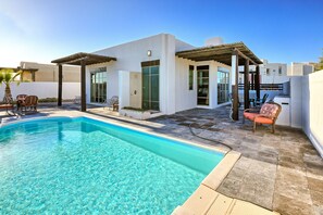 A modern outdoor pool area with a clear pool, a covered seating area, and a patio with chairs and a table. - Mayan Lakes Villa 52 – Private Pool, Resort Access (Puerto Penasco)