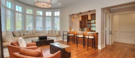 A spacious living room with a curved sofa, a coffee table, and a dining area with bar stools.