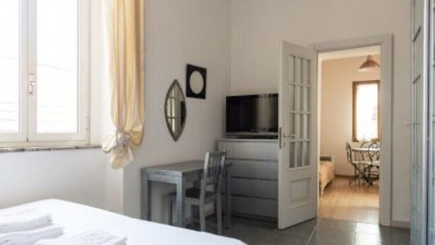 Une chambre d’hôtel comprenant un lit, un bureau, une chaise, un téléviseur et un coin repas, le tout visible à travers une porte ouverte.