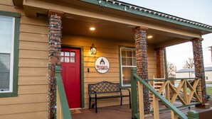 Un bâtiment en bois avec une porte rouge, un banc et une enseigne sur laquelle on peut lire : « La maison de Ralphie ».