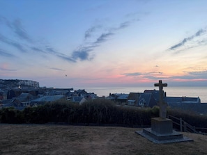 A coastal town at sunset with a prominent cross monument in the foreground.