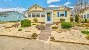 A two-story house with a front porch, a small garden with various plants and shrubs, and a clear blue sky.