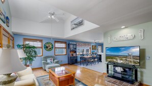 A spacious living room with a dining area, a kitchen in the background, and a large TV displaying a scenic view.