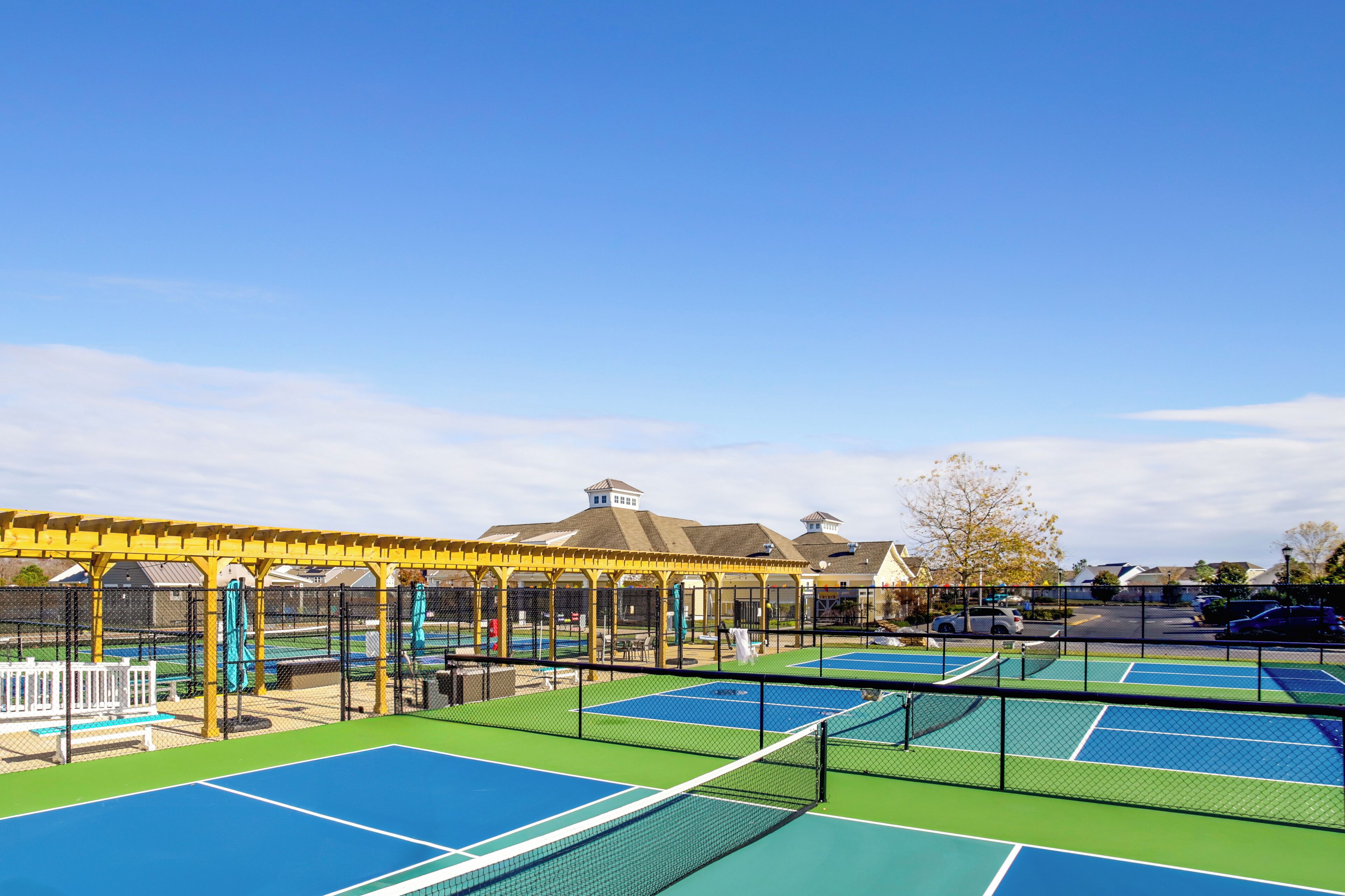 A tennis court complex with multiple courts, a covered seating area, and a building in the background.