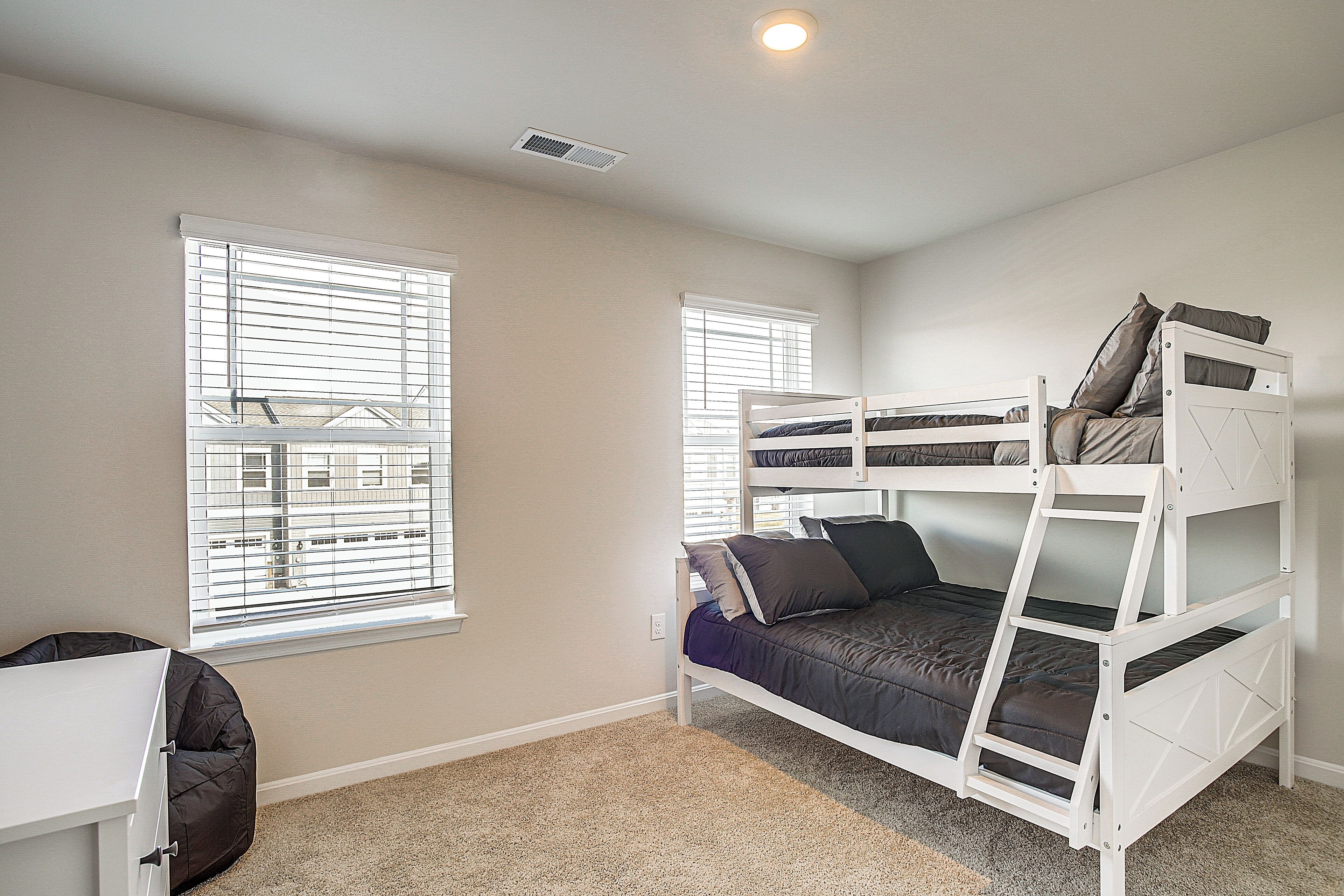 A bedroom with bunk beds, a desk, and a window with blinds.
