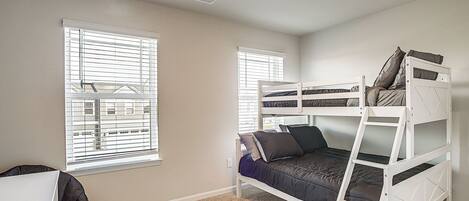 A bedroom with bunk beds, a desk, and a window with blinds.