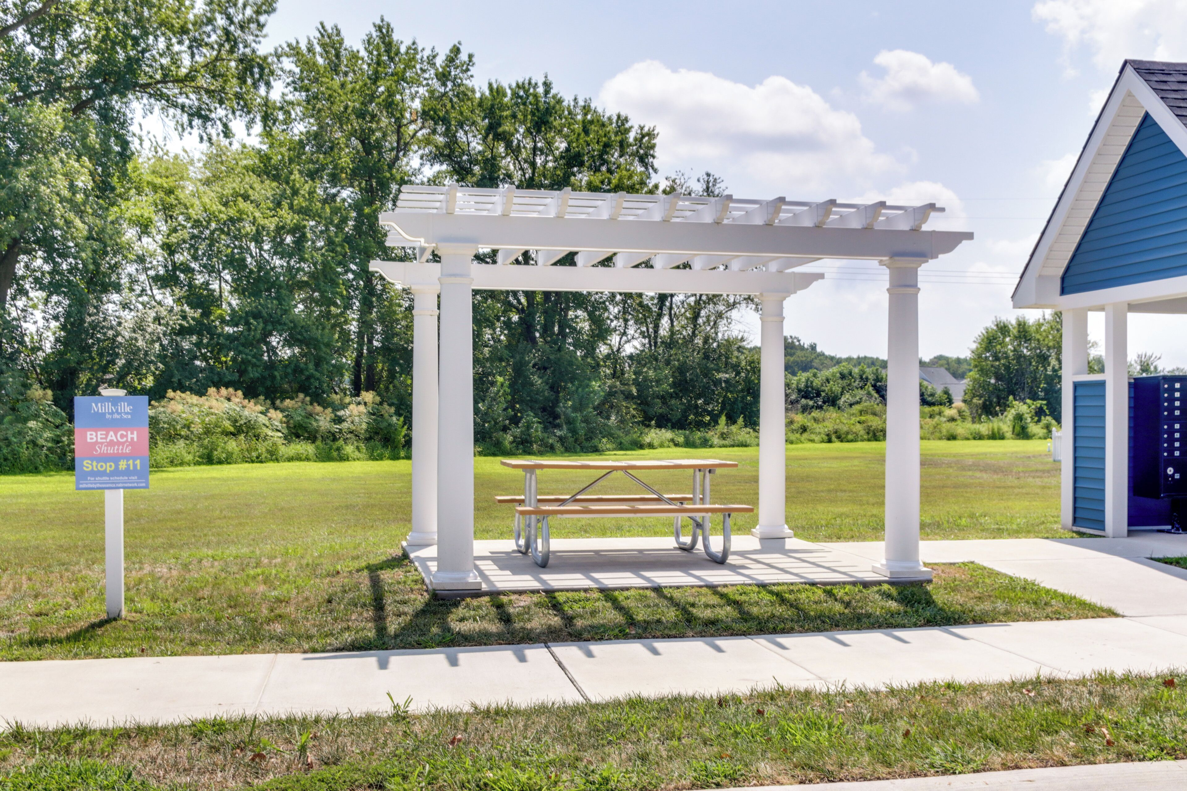 A gazebo with a picnic table, a sign for the Milville Beach Shuttle, and a blue building in the background.