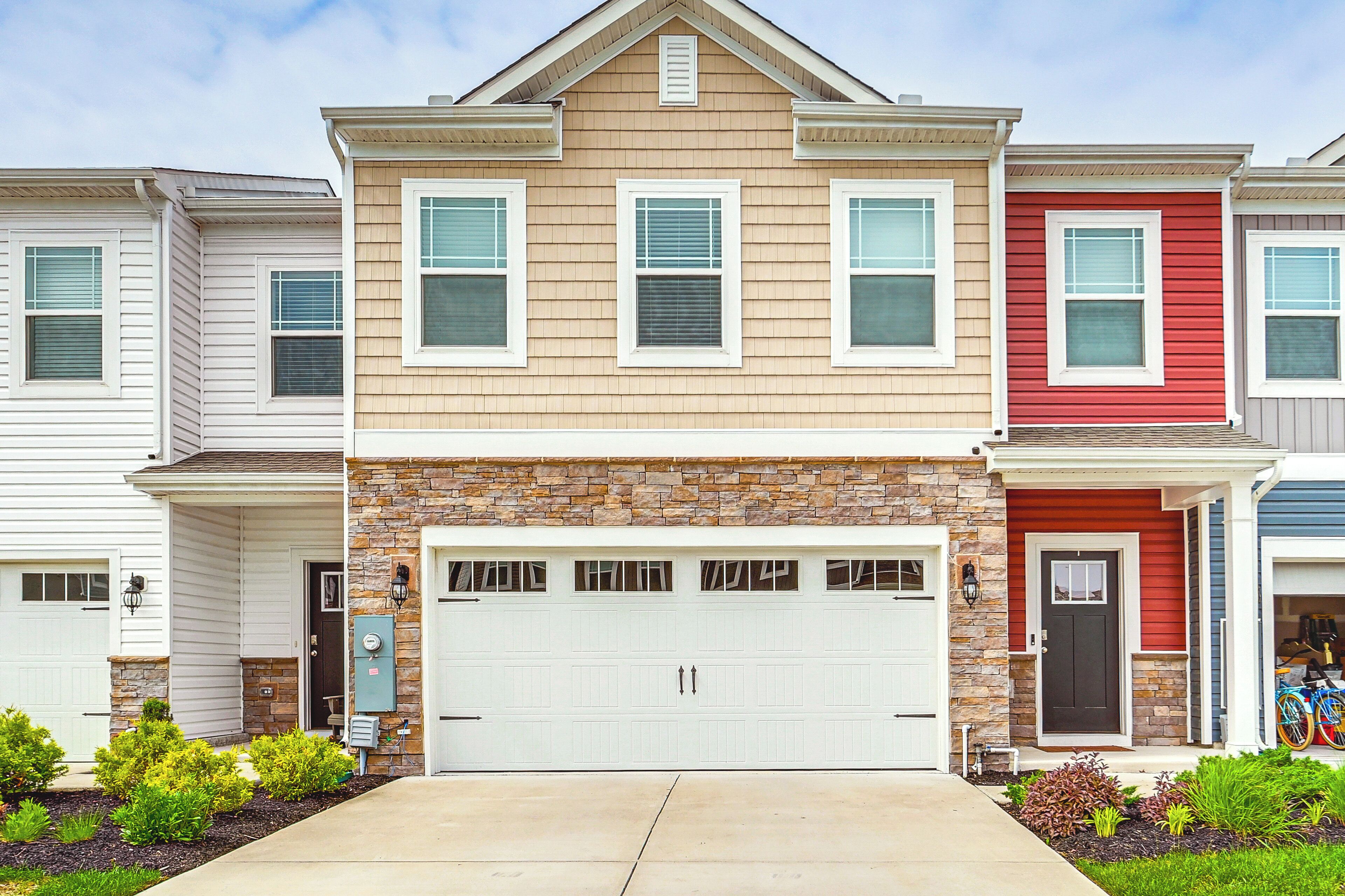 A row of townhouses with a central garage, stone accents, and a well-maintained front yard.
