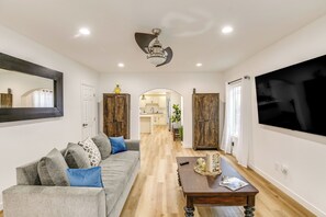Uma sala de estar moderna com um sofá cinzento, mesa de centro de madeira e uma grande tela de TV.
