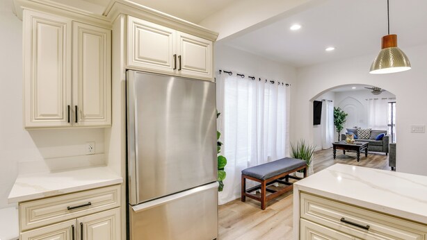 A modern kitchen with white cabinetry, a stainless steel refrigerator, and a marble countertop.